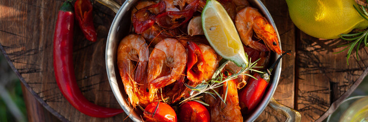 Romantic italian lunch outside of a couple: copper pan with delicious and spicy fried shrimps with herbs and garlic, bottle of olive oil, wine, bread. Luxury lifestyle, gourmet food. Banner