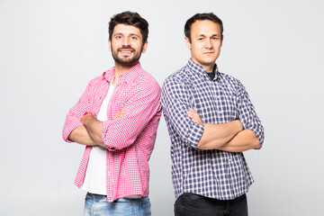 Portrait of a two smiling young men standing with arms folded back to back isolated over white...