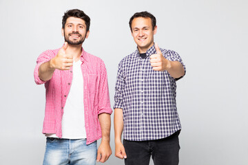 Two happy mens wearing casual t-shirt and jeans smiling and showing thumbs up on camera in studio...