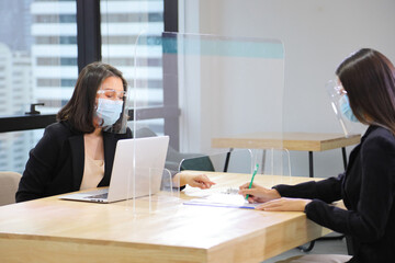Manager from HR department wearing facial mask is interviewing new applicant who is handing her...