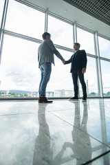 Full length side view of businessmen shaking hands in office building windows background