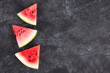 Fototapeta na wymiar Three triangular slices of fresh watermelon on a dark background. Summer still life, copy space for your text.