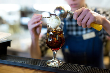 The bartender in the restaurant puts a ball of ice cream in a glass with a cocktail