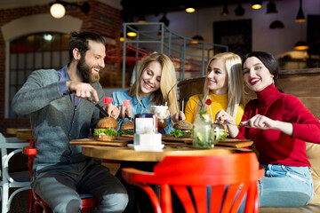 People have dinner together at a table in a cafe. Happy friends eat burgers and drink cocktails in the restaurant