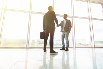 Two businessmen handshake in modern office with big panoramic windows