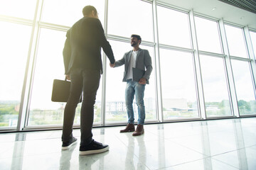 Two businessmen handshake in modern office with big panoramic windows