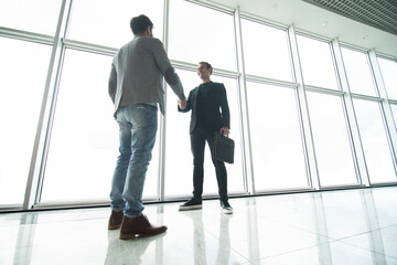 Two businessmen handshake in modern office with big panoramic windows
