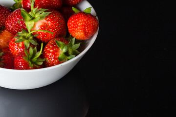 A few ripe strawberries lie on a deep white plate on black glass.Place for a copy of space
