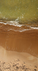 Top view of sea coast with soft waves and footprints on sand. Looking down at the Baltic sea beach.