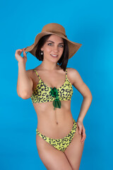 Portrait of a happy cheerful woman in a summer hat, leopard print swimsuit, isolated on a blue background. The concept of leisure and travel