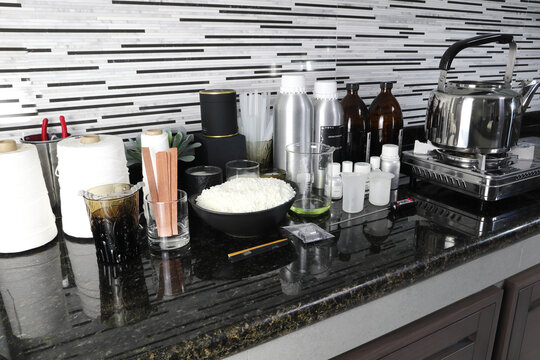 The Material Soy Wax, Fragrance And Essential Oil , Wick And Container Tools For Making Candle Are Put On The Marble Table Near The Gas Stove In The Kitchen Home