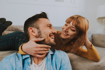 Fototapeta premium Young couple spending time together at home. Man and woman sitting on the couch and having fun.
