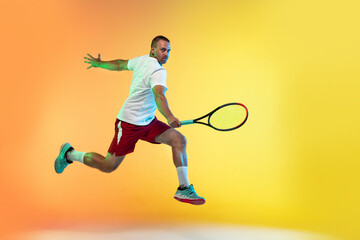 Fototapeta na wymiar In jump. One caucasian man playing tennis on studio background in neon light. Fit young professional male player in motion or action during sport game. Concept of movement, sport, healthy lifestyle.