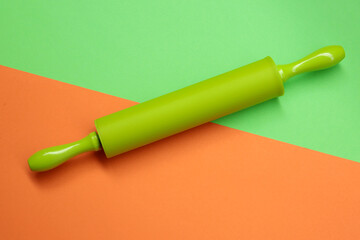 Big rolling pin in green color on green and orange backdrop.