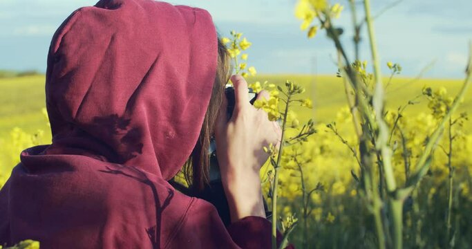 Close up side view of faceless woman photographing yellow field flowers on summer day. Unrecognizable female photographer shooting nature on vintage camera handheld device. Hobby profession