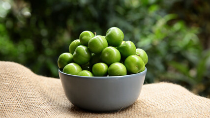 Green plums in a gray bowl in front of green leaves. summer fruit green plum. A hand picking a plum bowl.