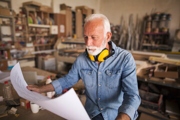 Elderly woodworker reading blueprint paper