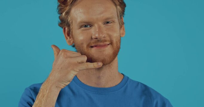 redhead man winking and showing call me gesture isolated on blue