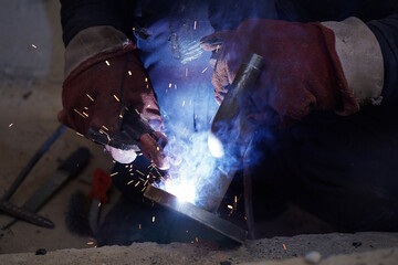 Close-up welder working with electrode at semi-automatic arc welding in manufacture production plant.Bright sparks from welding.