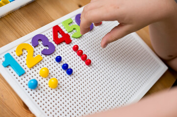 By provided numbers boy inserting pins. counting game. mathematical task. play at home. way of learning.