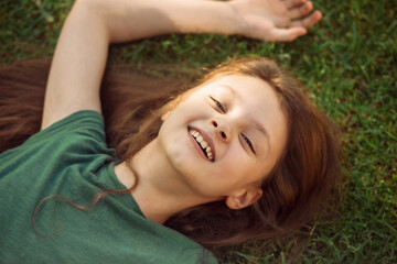 Obraz na płótnie Canvas Laughing playful kid girl lying on the grass on nature summer background. Closeup positive outdoors bright sunny