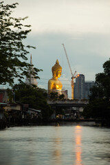 Big Buddha statue located by the river. And a boat was passing by : Pak Nam Phasi Charoen Temple, Bangkok, Thailand