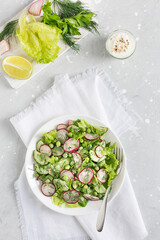 Fresh salad of cucumbers, radishes, green peas and herbs in white bowl. Top view. Vertical orientation