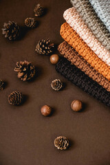 Fototapeta na wymiar Stack of knitted material from threads of brown, orange, gray colors with pine cones a brown background. Top view. Copy, empty space for text