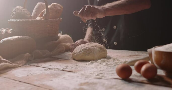Closeup shot of hands of senior bakery chef applying flour on dough, old man kneading dough, making bread using traditional recipe, isolated on black background 4k footage
