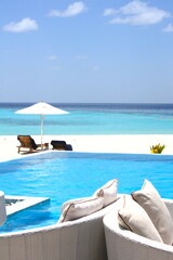 Fototapeta na wymiar Beautiful swimming pool with a tropical beach with a deckchairs on a white sand beach with turquoise blue water sea in background, in the turquoise of the laggon in an atoll of Maldives Islands.