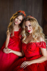 Obraz na płótnie Canvas Portrait of mother and daughter in luxurious red dresses and diadems. Mom touches her daughter's hair