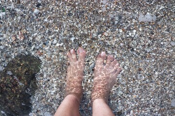 Stand on the beach, people feet in clear and beautiful of the sea.