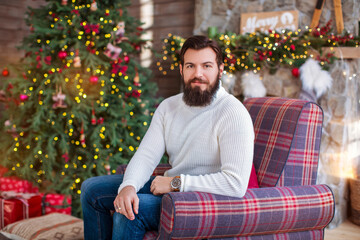 Warm and cozy christmas atmosphere at home.  Man bearded in sweater relax sit armchair near christmas tree. Feel like home.