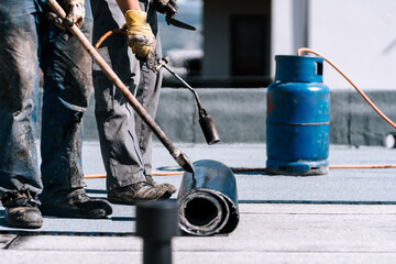 Fototapeta premium Rooftop terrace waterproofing details. Workers installing bituminous membrane waterproofing system insulation with blowtorch and tools
