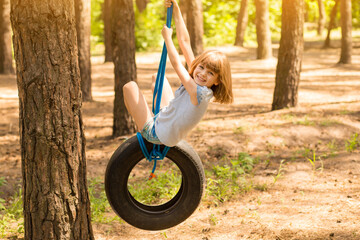 Happy active child girl playing on swing wheel in forest on sunny summer day. Preschool child...