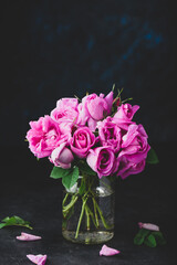 Small pink garden roses in jar on dark concrete background