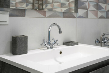 Modern bathroom interior with metal faucet and ceramic white sink. Bath accessories and mirror.