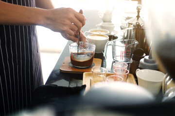 Asian barista young man making coffee according to order at counter bar with natural sunlight in the morning in modern cafe and restaurants.