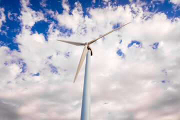 Tall, modern wind turbines spinning to generate renewable electricity with a cloud sky in the background.