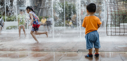 An adorable toddler Asian boy (1-year-old) standing and enjoy to see outdoor public fountains a water splashing for the first time