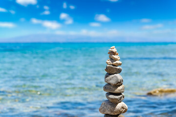Fototapeta na wymiar Closeup of Cairn of pebbles, Zen stack of stones on the sea stone beach under blue sky during sunny day in Greece