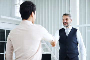 Smiling Senior Caucasian manager shaking hand with young Asain businessman after meeting and successful corporate in project