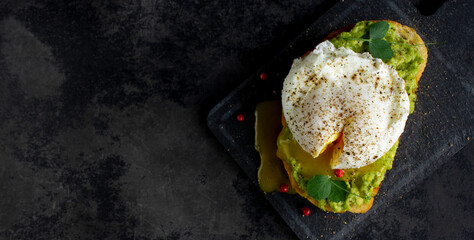 Top view of poached egg on avocado cream and bread toast on dark background with copyspace
