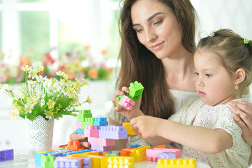 Obraz na płótnie Canvas Little daughter and happy mother playing with colorful plastic blocks