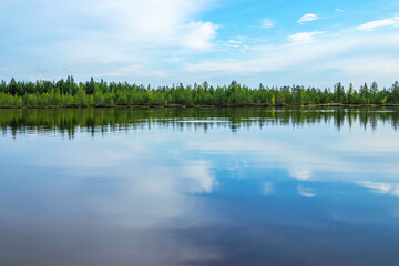 Landscape. Forest lake. The cloudy sky is reflected in clear water.