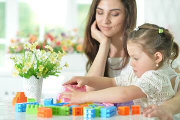 Obraz na płótnie Canvas Little daughter and happy mother playing with colorful plastic blocks