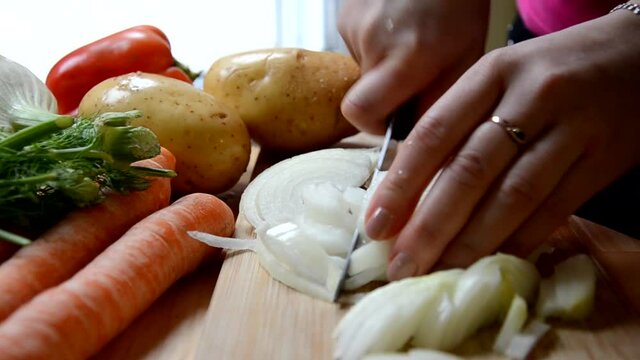 Girl chopping a onion with a knife on the cutting board. preparing to cook chicken soup or vegetable stew or salad