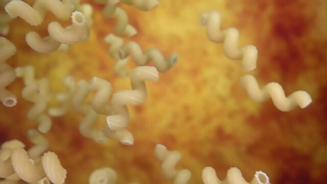  Dry pasta cellentani is falling diagonally on a yellow ochre background in slow motion