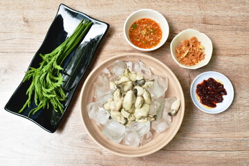 fresh oyster on ice in bowl eating couple acacia leaf and fried slice shallot dipping spicy sauce