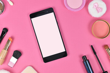 Flat lay with blank black smart phone with empty white screen surrounded by makeup beauty products...